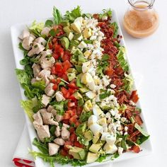 a salad on a plate with dressing next to it and a glass of orange juice