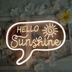 a neon sign that says hello sunshine on the side of a wall next to flowers