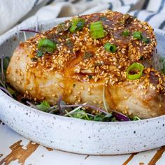 a white bowl filled with meat covered in sesame seeds and garnished with green onions