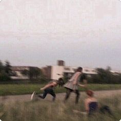 three people are running through the grass with a kite flying in the sky behind them