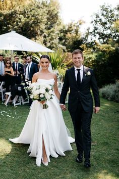 a bride and groom walking down the aisle at their outdoor wedding ceremony with an umbrella in the background