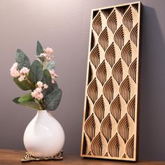 a white vase with some flowers in it on a table next to a wooden frame