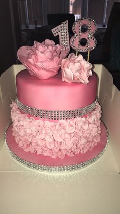 a three tiered cake with pink frosting and flowers on top is displayed in a box