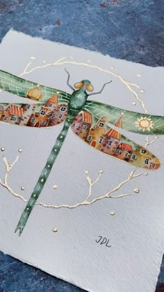 a painting of a dragonfly sitting on top of a white piece of paper with houses in the background