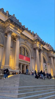 many people are sitting on the steps in front of a large building with columns and windows