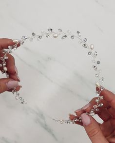 two hands are holding pearls and beads on a white marble surface, while the other hand is wearing a silver bracelet