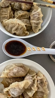 two white bowls filled with dumplings next to chopsticks on a gray table