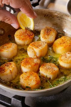 someone is cooking scallops in a pan with lemon wedges on the side