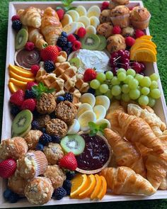 a platter filled with croissants, fruit and pastries on top of green grass