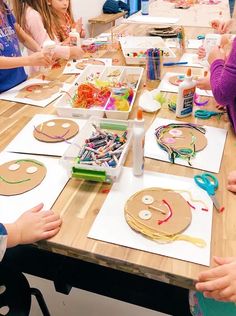 a group of children sitting at a table making art projects with paper plates and scissors