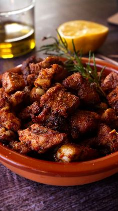 a bowl filled with fried food next to a glass of olive oil and lemon wedges