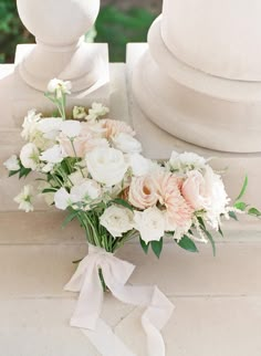 a bouquet of white and pink flowers sitting on top of a stone bench next to a pillar