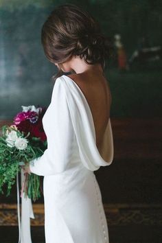 a woman in a white dress is holding a bouquet and looking down at the ground