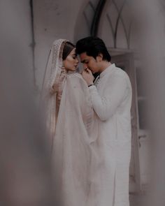 a man and woman standing next to each other in front of a church door, dressed in white