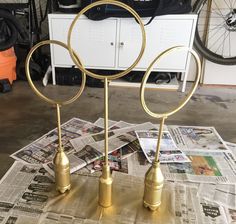 three brass rings on top of newspapers in front of a white cabinet and bicycle rack