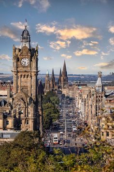 a large clock tower towering over a city with tall buildings on both sides and trees in the foreground