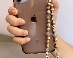 a person holding an iphone in their hand with beaded bracelets attached to it