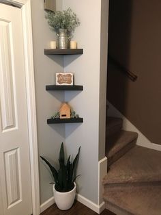 three shelves with plants and candles on them in the corner of a room next to stairs