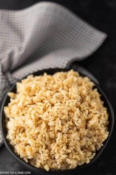 brown rice in a black bowl next to a white towel and napkin on a dark surface