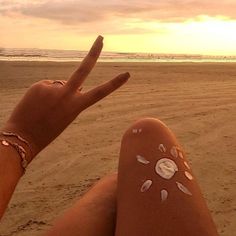 a person sitting on the beach with their hand painted like a peace sign and shells