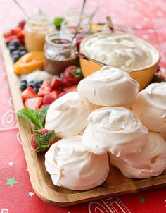 a wooden tray topped with whipped cream and fruit on top of a red table cloth