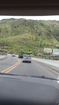 two cars driving down the road in front of a green hill with signs on it