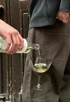 a man pouring white wine into a glass in front of an open door with his hand