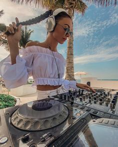 a woman wearing headphones is playing music on a turntable at the beach with palm trees in the background