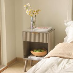 a bed with a white comforter and a wooden side table holding two green apples