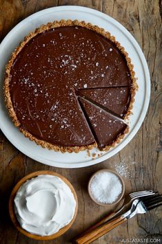 a chocolate pie on a white plate next to some whipped cream and two spoons