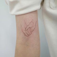 a woman's arm with a small tattoo on her left wrist, holding the hand of another person