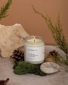 a candle sitting on top of a table next to some rocks and pine cones in front of a rock