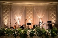 a stage set up with flowers and musical instruments in front of the curtained wall