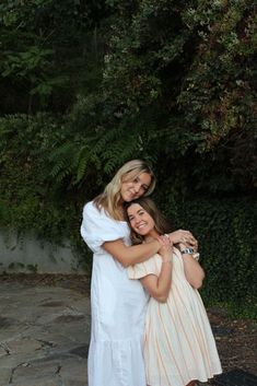 two women hugging each other in front of trees