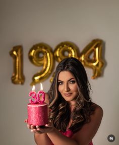 a woman holding a pink birthday cake with the number forty nine on it and gold balloons behind her