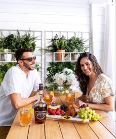 two people sitting at a table with drinks and fruit