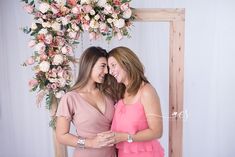 two beautiful women standing next to each other in front of a floral arch with pink and white flowers