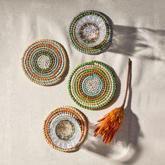 three decorative plates on a white surface with orange tassels next to one another