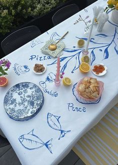 a white table topped with plates and bowls filled with food on top of a blue and white table cloth