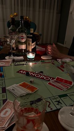 people sitting at a table with drinks and cards on it in front of a bottle