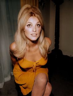 a woman sitting on the floor with her legs crossed in front of her face and wearing an orange top