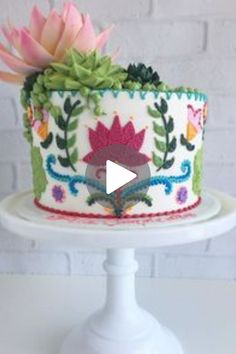 a decorated cake with flowers on it sitting on top of a white pedestal next to a brick wall