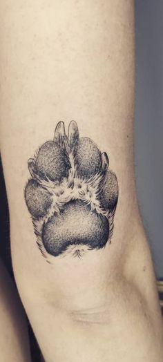 a black and white photo of a dog's paw tattoo on the right thigh