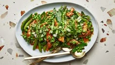 a white plate topped with asparagus covered in sauce next to two spoons