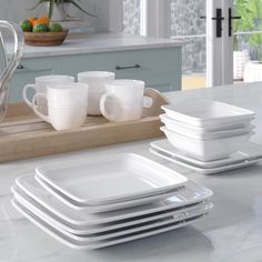 a set of white dishes and cups on a kitchen counter with an oven in the background