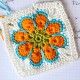 an orange flower is on top of a white doily with blue and green trim