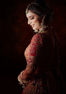 a woman in a red and gold dress with jewelry on her head, standing against a dark background