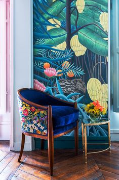 a blue chair sitting in front of a wall with flowers and plants painted on it