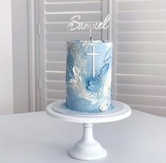 a blue cake with white frosting and a cross on top is sitting on a table