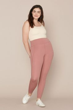 a woman standing in front of a wall wearing pink pants and white top with her hands on her hips